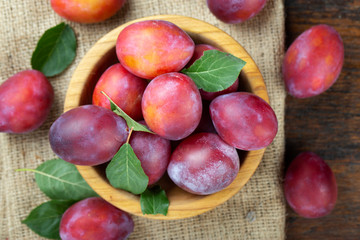 Wooden plate with ripe juicy plums on table.