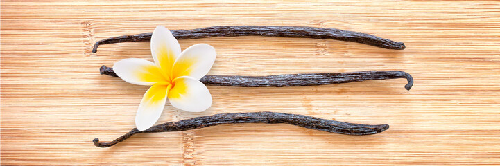Three vanilla pods with a flower aligned on wooden panoramic background