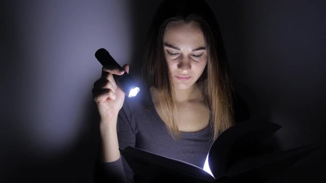 portrait of a girl close up she sits with a flashlight and turns the pages of a book in a dark room