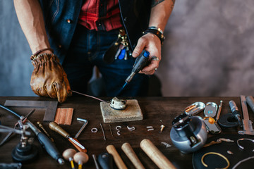 man in gloves melting silver to make jewelry, close up cropped photo