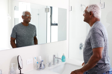 Obraz premium Smiling Senior Man Looking At Reflection In Bathroom Mirror Wearing Pajamas