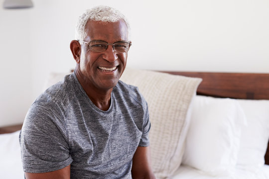 Portrait Of Smiling Senior Man Sitting On Side Of Bed At Home Looking Positive