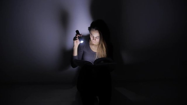 close-up portrait girl is reading a book with a flashlight in a dark room at night. 4k. Motion shooting