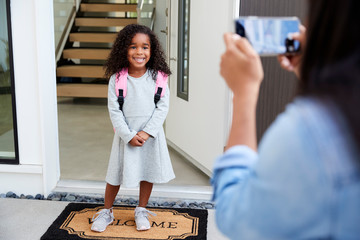 Mother Taking Photo Of Daughter With Cell Phone On First Day Back At School
