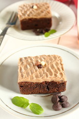 Chocolate bakery style cake brownie  with chocolate cream on top on a white plate and mint leaf and a glass of milk in the background