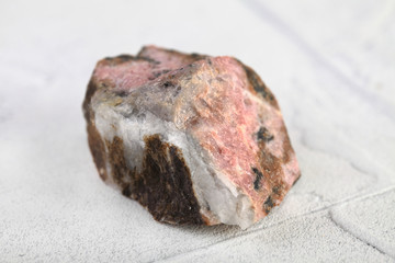 Natural mineral rock specimen - rough rhodonite stone from M. Sidelnikovo, Ural, Russia on white cement background.