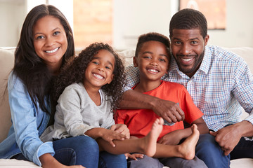 Portrait Of Family Sitting On Sofa At Home Smiling At Camera