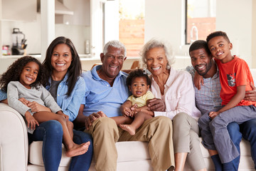 Portrait Of Multi-Generation Family Sitting On Sofa At Home Smiling At Camera
