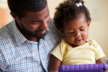 Obraz premium Baby Daughter And Father Playing With Toy On Sofa In Lounge At Home