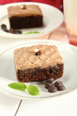 Chocolate bakery style cake brownie  with chocolate cream on top on a white plate and mint leaf and a glass of milk in the background