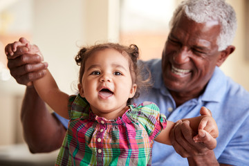 Portrait Of Smiling Grandfather Sitting On Sofa At Home With Baby Granddaughter