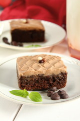 Chocolate bakery style cake brownie  with chocolate cream on top on a white plate and mint leaf and a glass of milk in the background