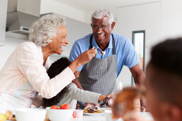 Grandparents In Kitchen With Granddaughter Making Pancakes Together