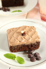 Chocolate bakery style cake brownie  with chocolate cream on top on a white plate and mint leaf and a glass of milk in the background