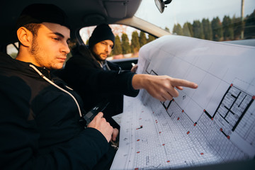 Two robbers planning and pointing on the blueprint(map) their objective while holding their guns.