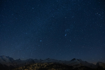 Herrliches Sternenmeer mit tintenblauem Himmel in klarer Nacht über schneebedeckten Bergen in...