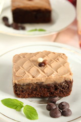 Chocolate bakery style cake brownie  with chocolate cream on top on a white plate and mint leaf and a glass of milk in the background