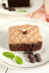 Chocolate bakery style cake brownie  with chocolate cream on top on a white plate and mint leaf and a glass of milk in the background