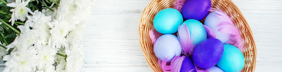 Basket with colored eggs and flowers on wooden background. Top v