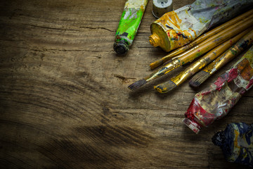 Old paint tubes and brushes on wooden background 
