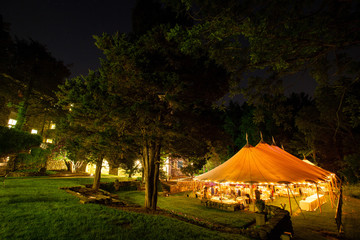 a wedding tent at night surrounded by trees with an orange glow from the lights. - wedding tent...