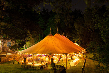 a wedding tent at night surrounded by trees with an orange glow from the lights, long exposure -...