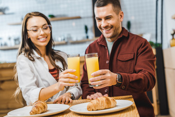selective focus of glasses with juice in woman and man hands sitting at table with croissants in coffee house
