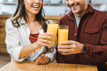 cropped view of woman and man sitting at table and clinking glasses with juice in coffee house