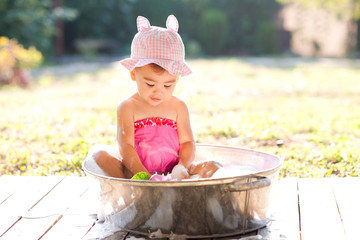 Cute baby girl taking bath outdoors. Playing in bathtub with soap foam.
