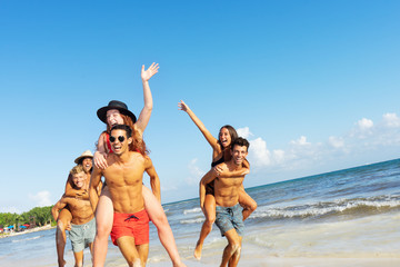 Happy group of young friends doing piggyback ride at the beach. Dutch angle