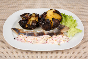 Baked potatoes and herring with sauce and salad on a white plate.
