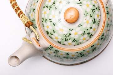 Closeup of a beautiful decorated teapot kettle with flower motif and straw wooden handle. Studio shot of a kettle on a white background filling the frame.