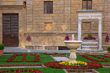 Fototapeta na wymiar Old well in the main square of Pienza. The travertine well of the Rossellino and the front of Palazzo Piccolomini in Pienza, Tuscany, Italy