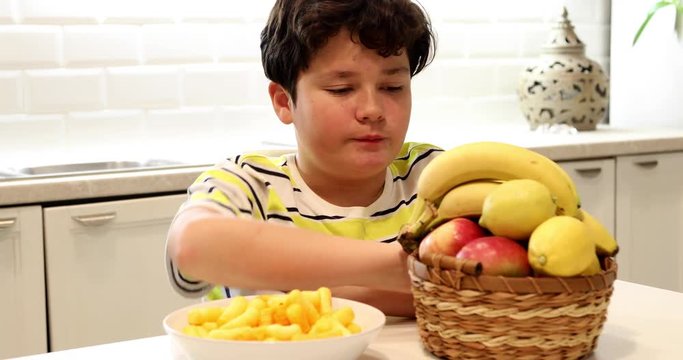 Teen boy choosing between fruits and chips 4