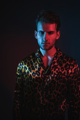 Art neon glamor fashion men's model tests. Handsome guy model posing in leopard shirt on a blue and red filter. Fashion photography in the studio.