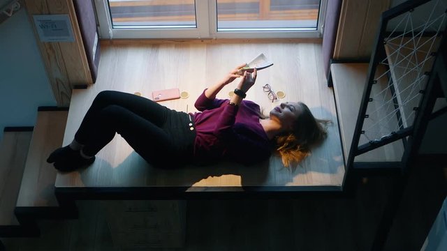 Woman is reading a book lying on the stairs by the window. Escape of reality.