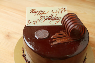 Creamy white chocolate birthday greeting card topped on chocolate mousse cake on the wooden table