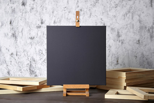 Black blank cotton canvas for acrylic and oil paints, a wooden easel and stretcher bars on table