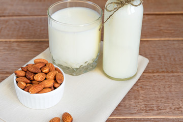 Homemade Almond milk in a bottle and nuts in white porcelain bowl on wooden background