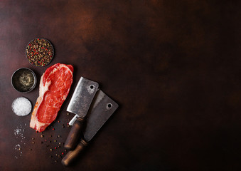 Raw sirloin beef steak with vintage meat hatchets on rusty background. Salt and pepper with fresh rosemary and bowl of oil.Space for text