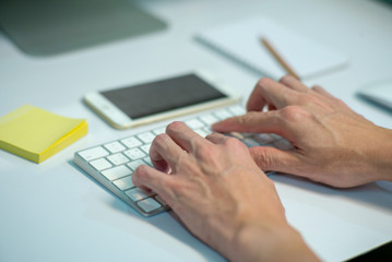 Fototapeta na wymiar Closeup selective focus on hands of businessman typing on the keyboard with defocused stationaries and mobile phone in background