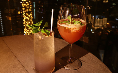 Two glasses of different type of cocktail at the rooftop bar with bokeh lights in background 