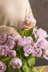 Florist at work: pretty young woman making a big bouquet of double violet tulip flowers on a dark rustik background