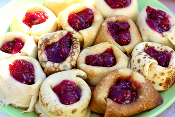 Thin ruddy pancakes on milk with cherry jam, wrapped rolls. Pancakes are packed tightly on a large dish. Pancake week. Pancakes for breakfast and carnival. Homemade baking.