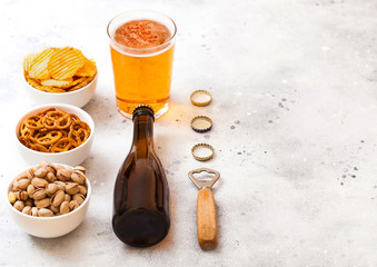 Glass and bottle of craft lager beer with snack and opener on stone kitchen table background. Pretzel and crisps and pistachio in white ceramic bowl. Space for text