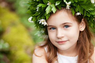 Beautiful  little girl in a white dress  in the spring wood. Portrait of the pretty little girl with a wreath from spring flowers on the head. Easter time