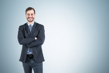 Obraz na płótnie Canvas Smiling businessman with crossed arms, gray wall