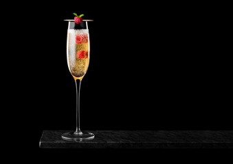 Elegant glass of yellow champagne with raspberries and bubbles inside black marble board on black background.Space for text