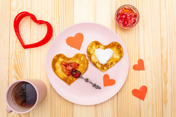 Naklejka na ściany i meble Heart shaped pancakes for romantic breakfast with strawberry jam and black tea. Shrovetide (carnival) concept. On wooden background, top view