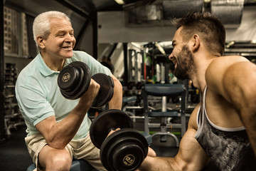 Fototapeta na wymiar Professional fitness trainer helping his senior client exercising with dumbbells